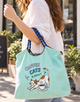 Woman in a white top carrying a mint green Coffee Cats tote bag on her arm while walking outdoors.