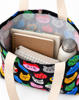 A colorful cat face tote bag is shown open with notebooks, a pencil case, and a water bottle inside, showing its roomy interior.