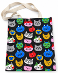 A tote bag with a black background and a colorful repeating pattern of cartoon cat heads in various colors, featuring natural beige shoulder straps.