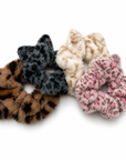 Four soft, fluffy cat ear scrunchies in brown leopard, gray and black leopard, cream leopard, and pink leopard designs.