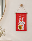 A Lucky Cat wall hanging displayed on a bright interior wall.