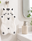 White cat-shaped hand towel with black embroidered details hanging from a wall hook beside a bathroom sink.