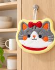 Cat face hanging hand towel displayed on a wooden kitchen cabinet.