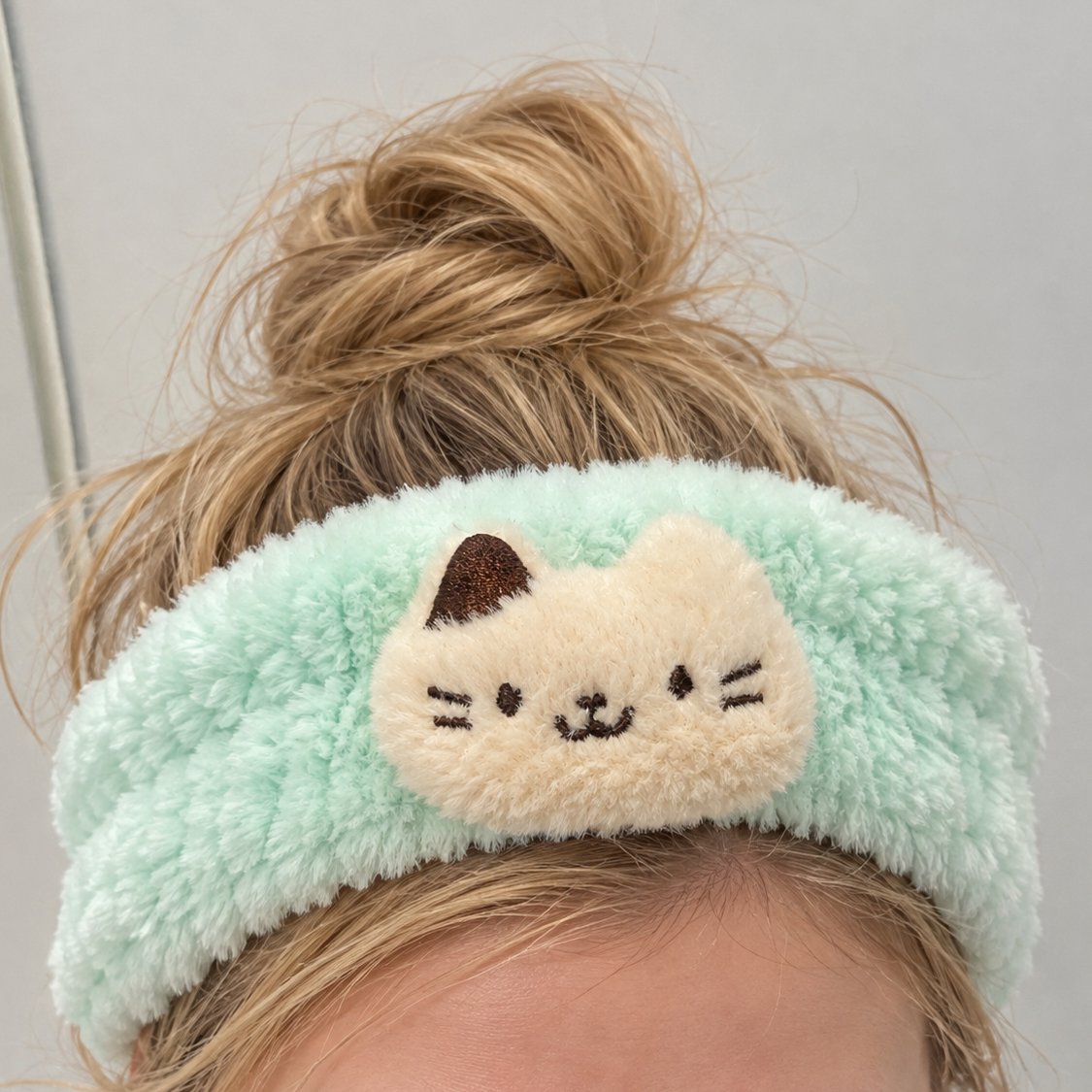 Mint green fluffy cat spa headband worn with hair tied up, featuring a cream cat appliqué.