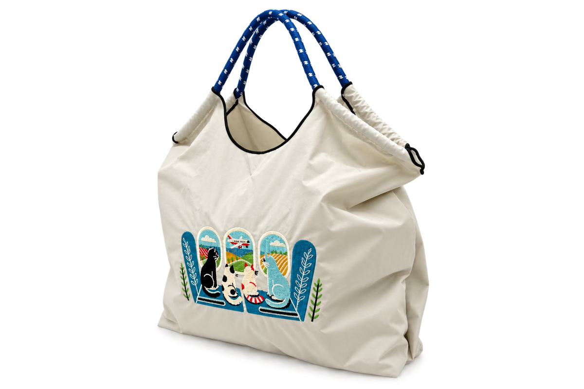 Angled side view of a gray Cats by the Window foldable tote bag filled with items, showing its roomy shape and blue rope-style handles.