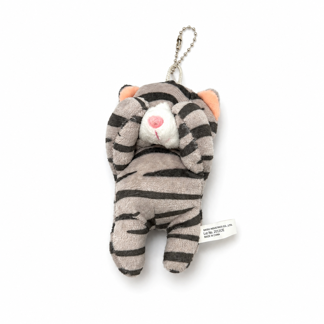 A gray tabby cat plush charm with its paws covering its eyes, a white muzzle, pink inner ears, and a pink nose, attached to a silver ball chain.