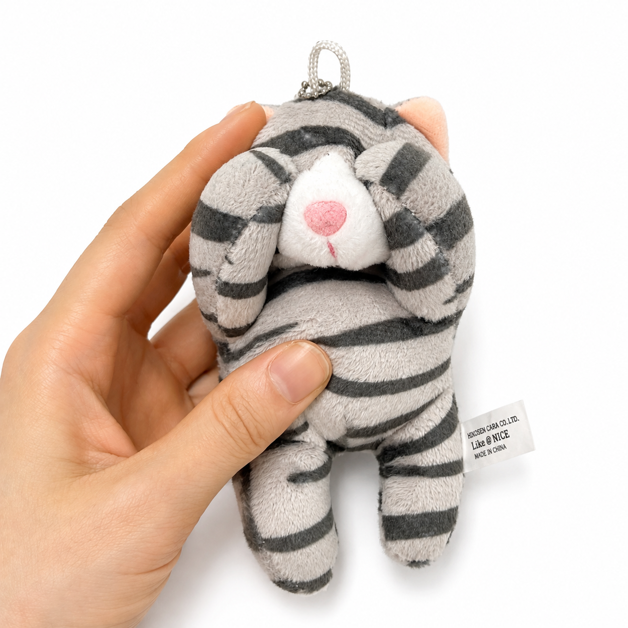 A gray tabby cat plush charm with a silver ball chain, held in a person's hand to show its size.