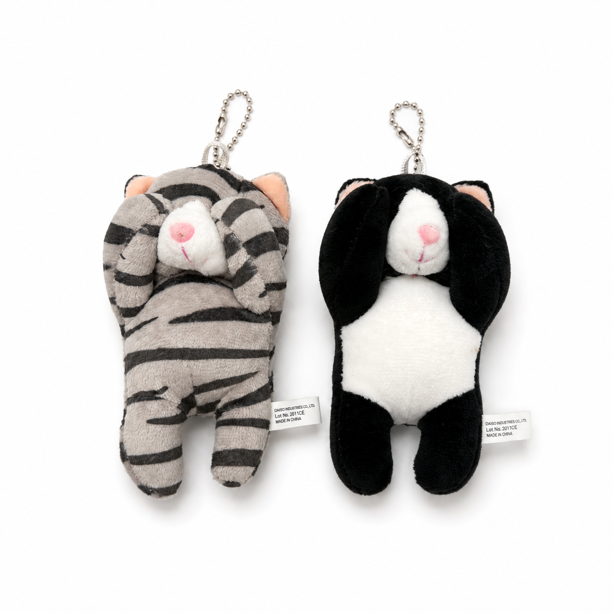 Two cat plush charms displayed side by side, one a gray tabby stripes and the other a tuxedo cat, both designed with their paws covering their eyes and attached to silver ball chains.