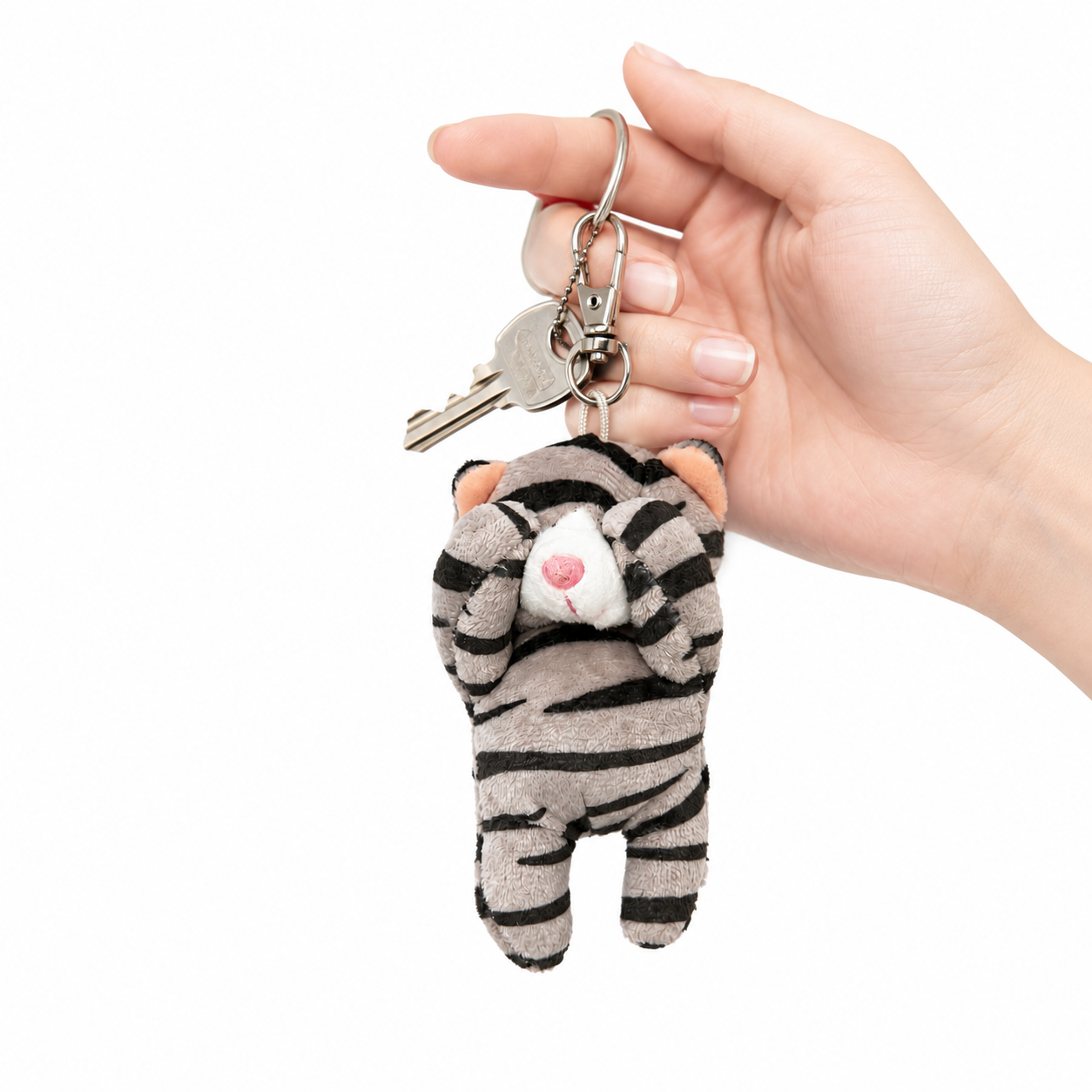 A gray tabby cat plush charm with its paws covering its eyes, attached to a key ring with keys, held in a person's hand.