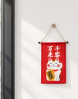 A red Lucky Cat wall hanging banner is displayed on a bright wall near a window.