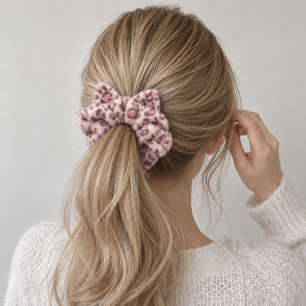 Woman wearing a soft, fluffy pink leopard-print cat ear scrunchie in a ponytail.
