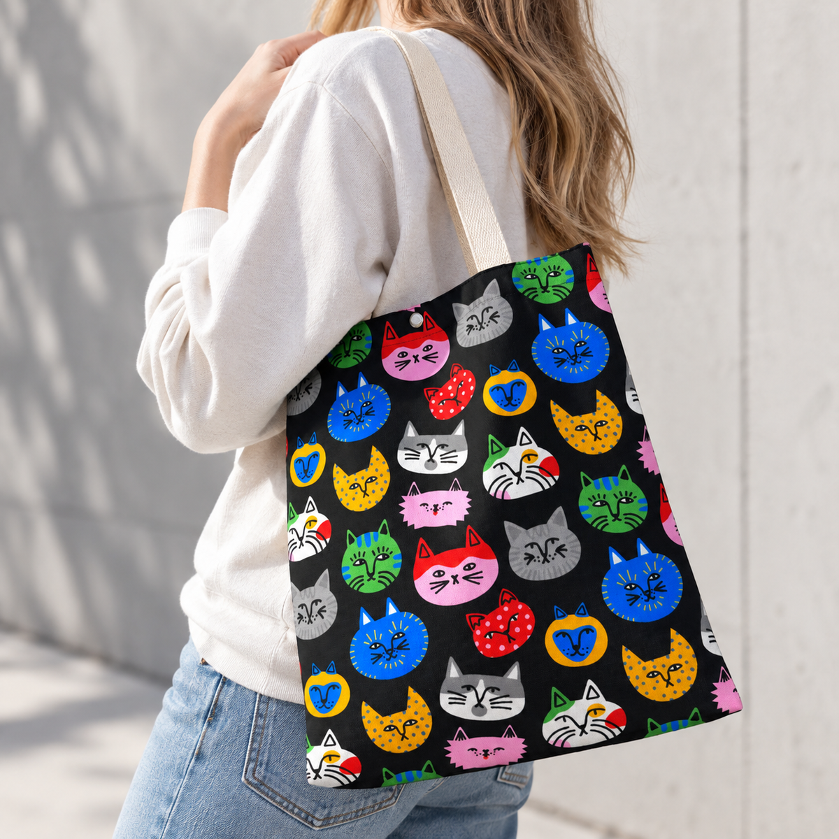 A woman is carrying a colorful cat face tote bag over her shoulder while walking outdoors.