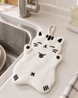 White cat-shaped hand towel with black embroidered details placed beside a kitchen sink.