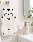 White cat-shaped hand towel with black embroidered details hanging from a wall hook beside a bathroom sink.